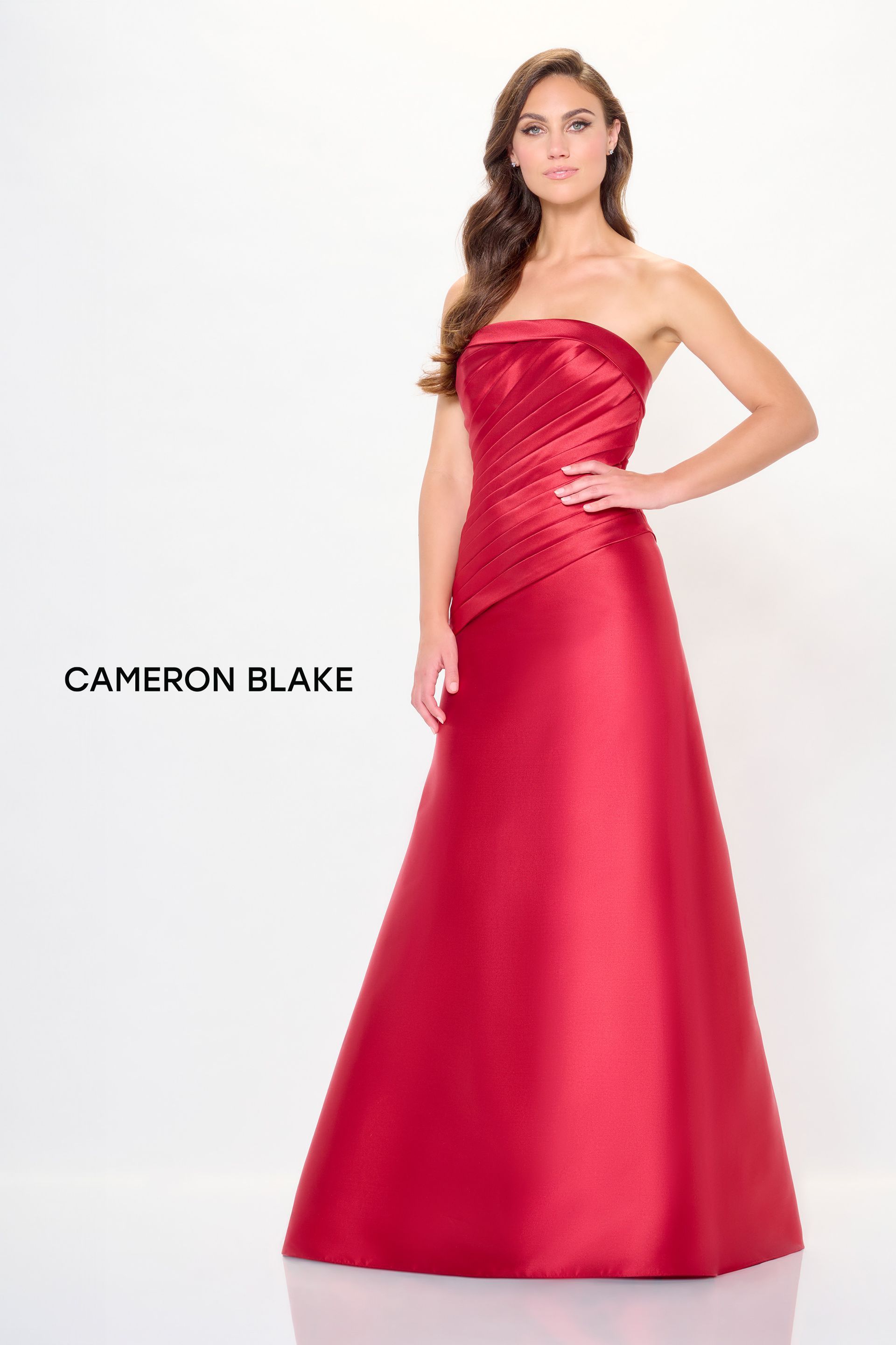 Woman in a red strapless gown, posed in a studio setting. Dress has pleated bodice.