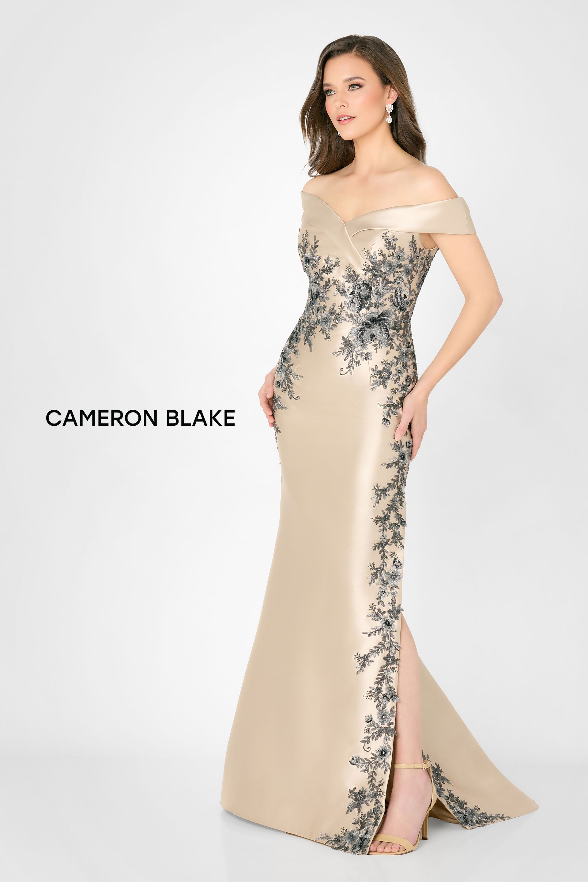 Beige off-shoulder evening gown with black floral side detail and thigh slit on a white background