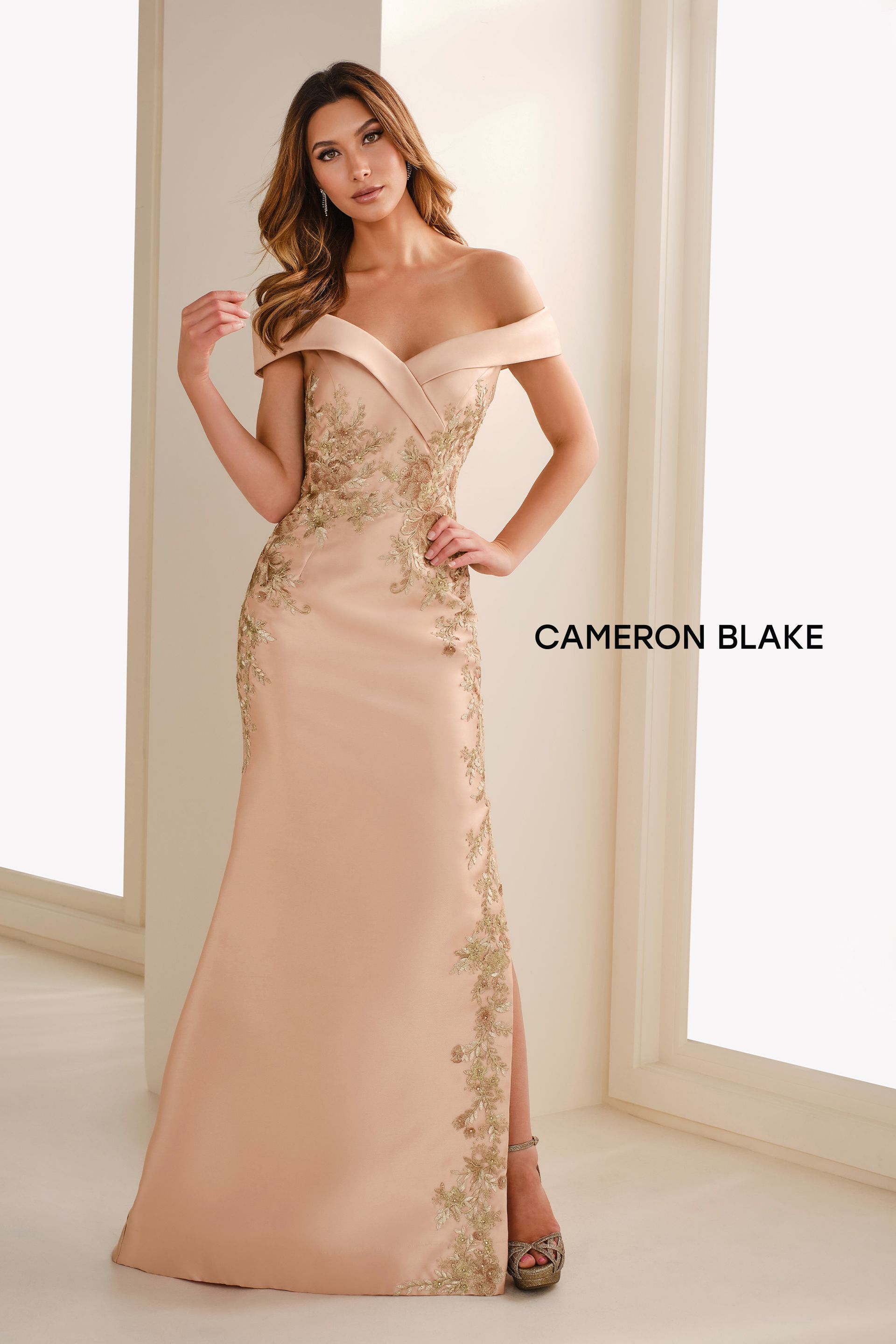 Beige off-shoulder evening gown with black floral side detail and thigh slit on a white background