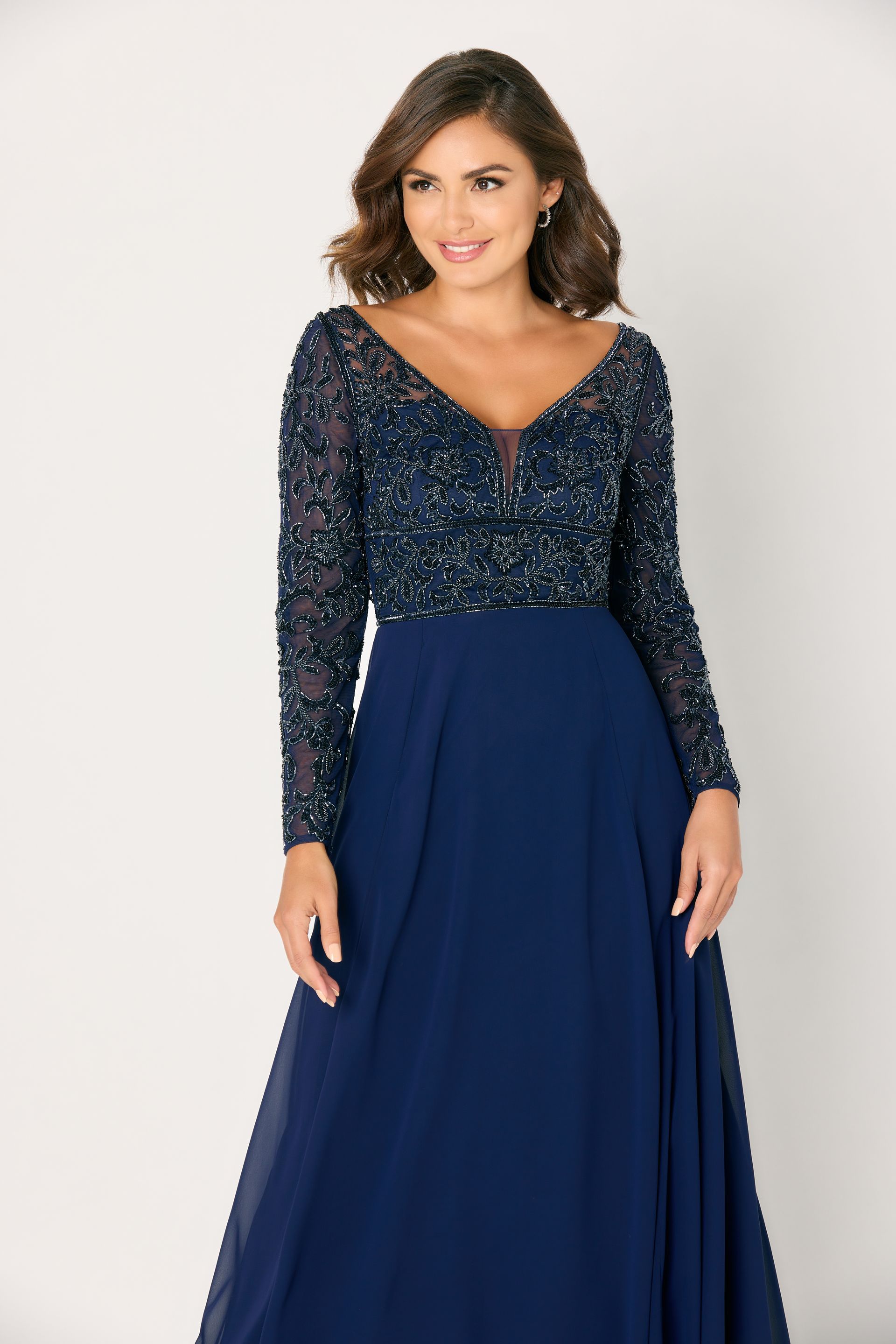 Woman in a navy blue formal gown with a beaded bodice, smiling. White background.