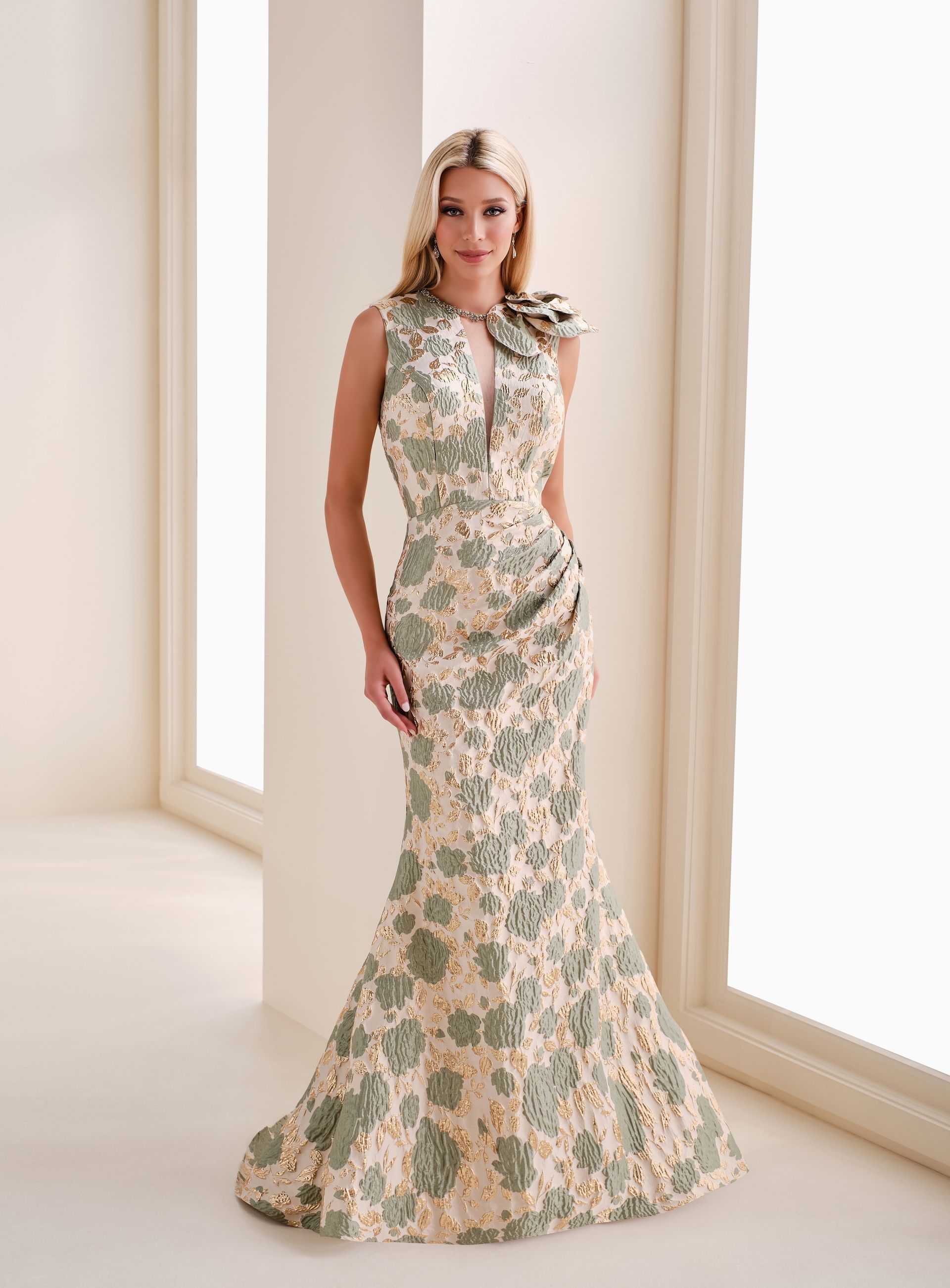 Woman in a floral patterned formal gown, standing near a window.