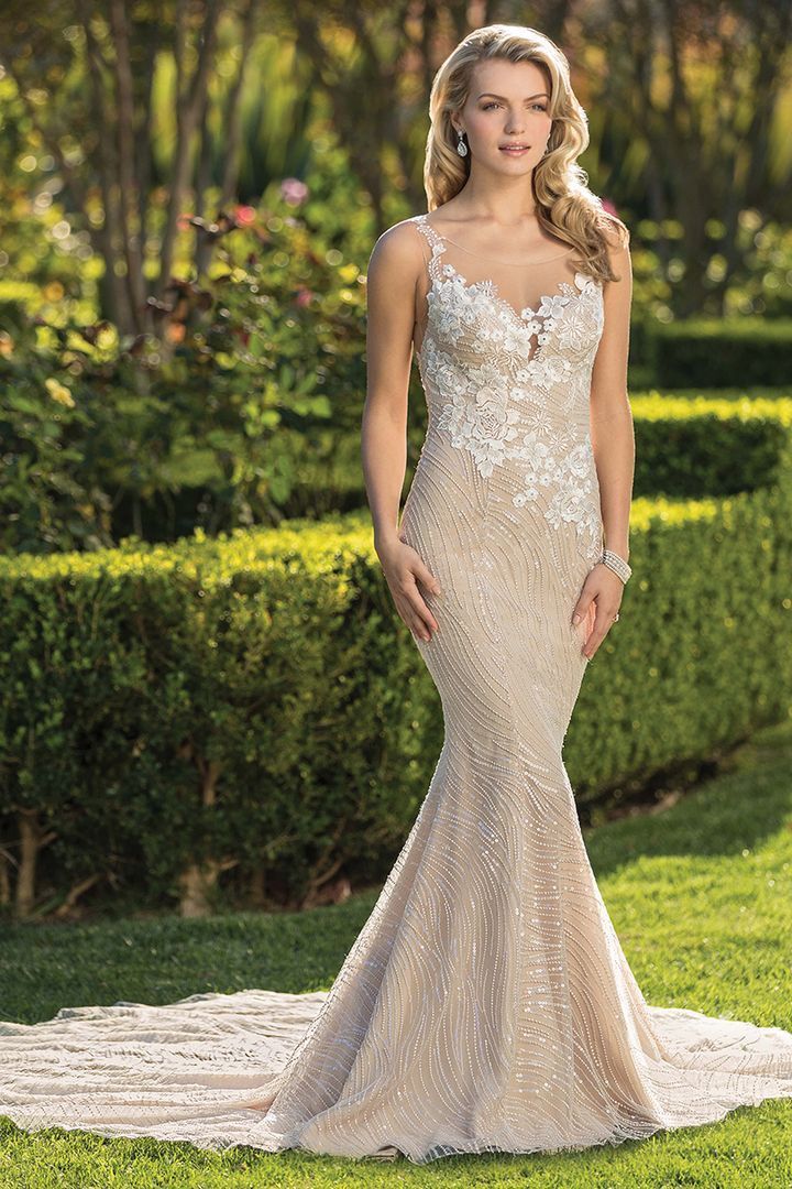 Woman in a beaded, champagne-colored mermaid-style wedding gown, standing in a garden.