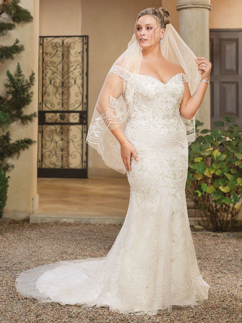 Woman in a white, beaded mermaid wedding dress with a veil, standing outside near a wrought iron door.