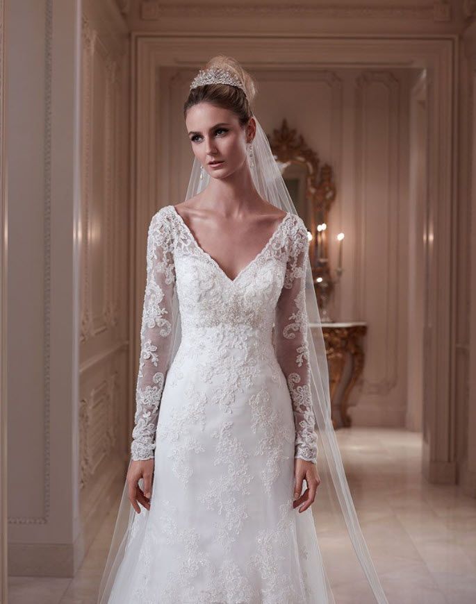 Woman in white lace wedding dress with veil, standing in elegant hallway.