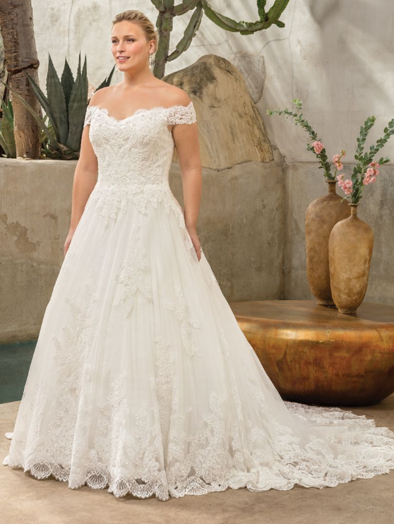 Woman in off-the-shoulder lace wedding dress, standing outdoors.