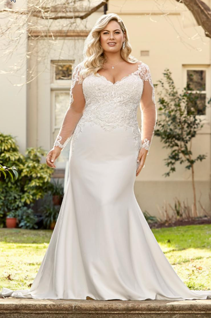 Woman in white wedding dress with lace sleeves, standing outdoors.
