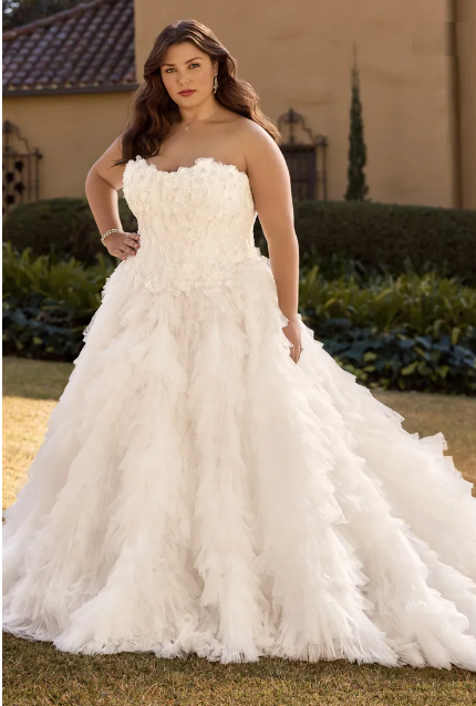 Woman in a white strapless wedding gown with ruffled skirt, posing outdoors.