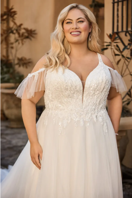 Woman in a white wedding dress with off-the-shoulder sleeves, smiling outdoors.