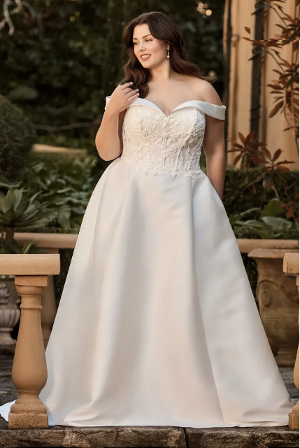 Woman in a white off-the-shoulder wedding gown poses outdoors.