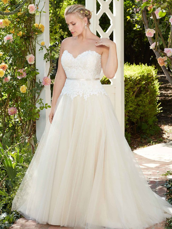 Woman in a strapless ivory wedding dress, standing outdoors by an arbor with roses.