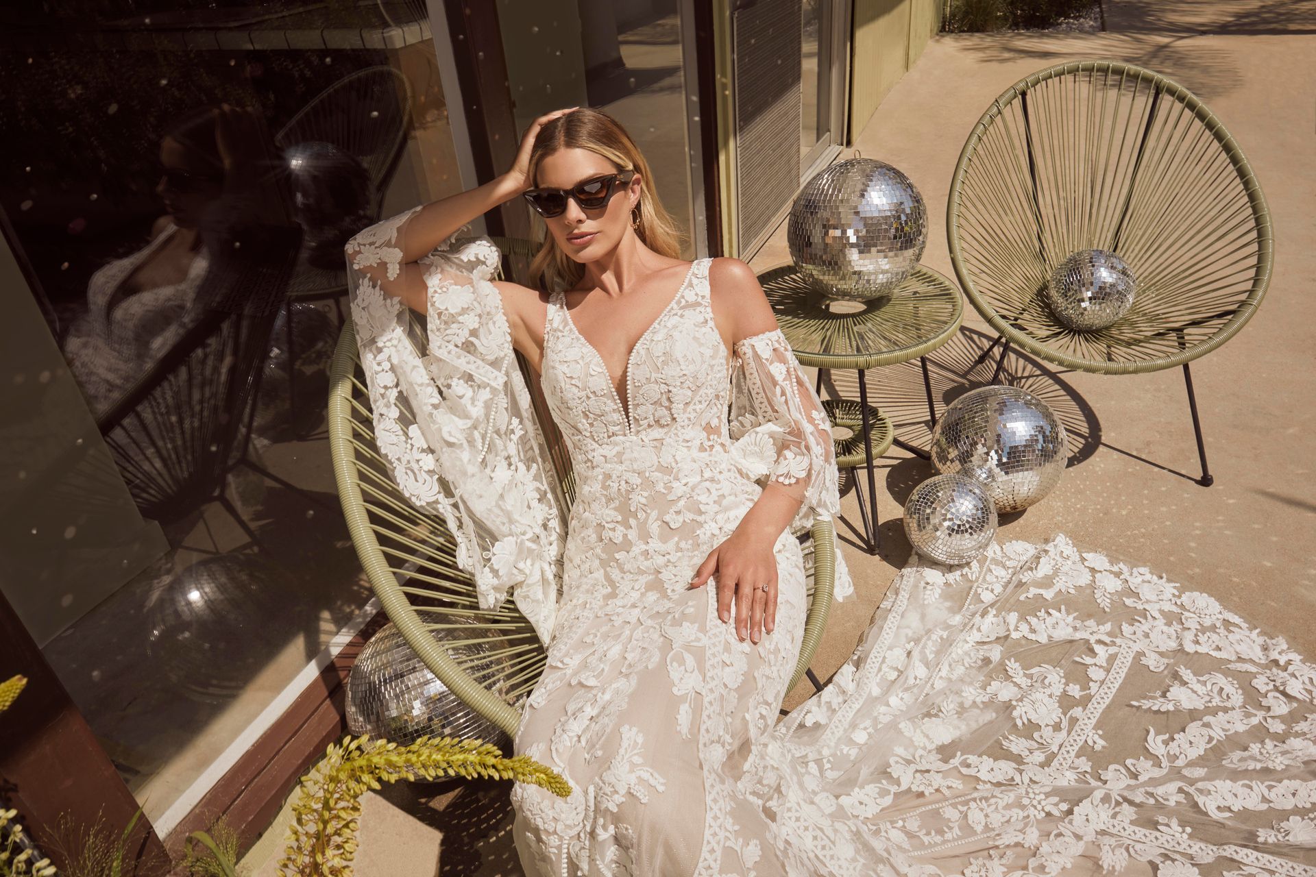 Woman wearing a white lace wedding dress, sunglasses, sitting in a green chair, with disco balls.