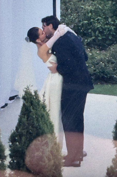 Couple kissing on their wedding day, embracing outside. Woman in white dress, man in a dark suit.