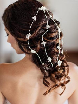 Woman with dark hair in an updo, adorned with a floral hairpiece; focus on the back, indoor setting.