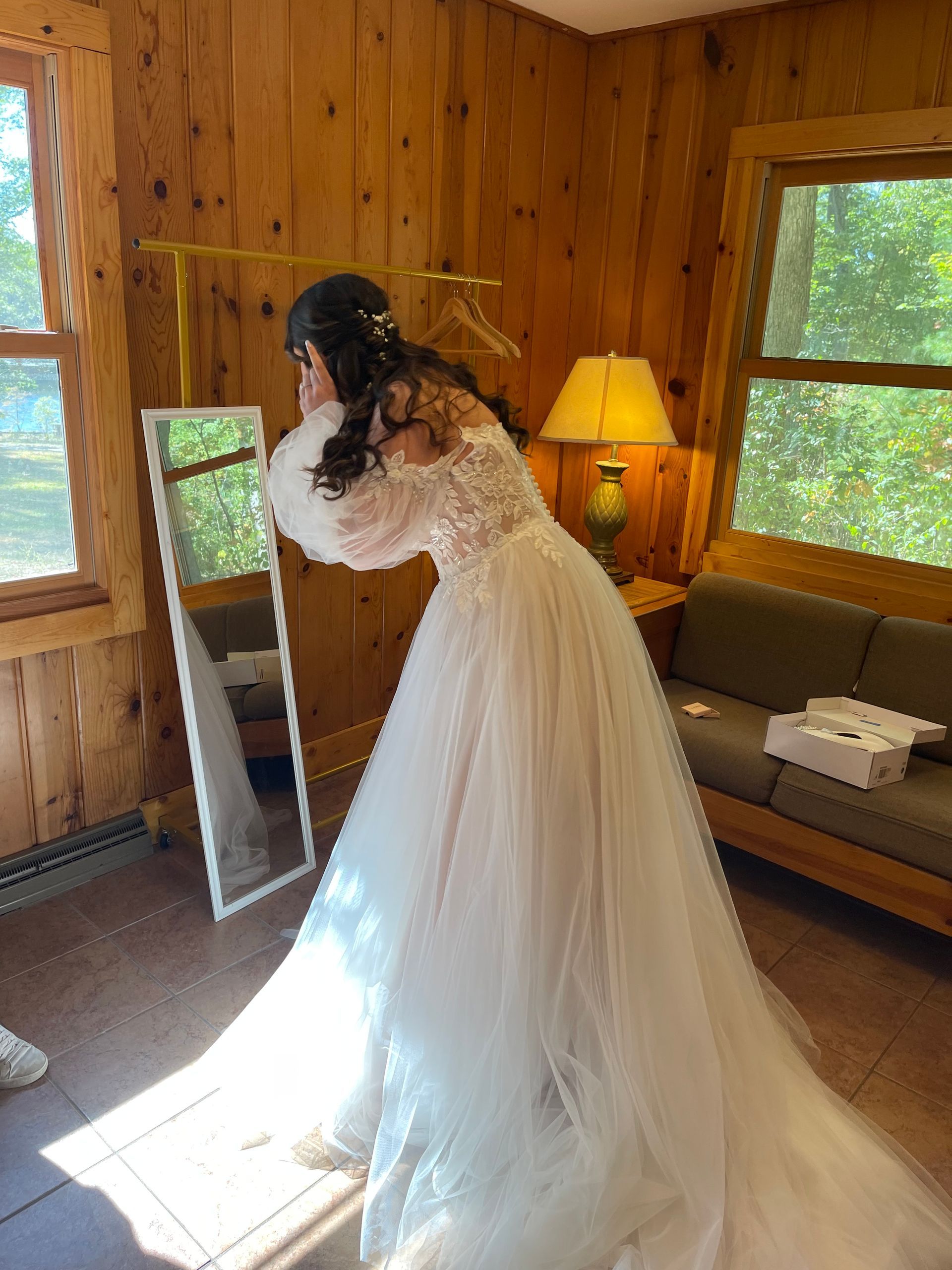 Bride in a white wedding dress admires herself in a mirror, in a wood-paneled room.