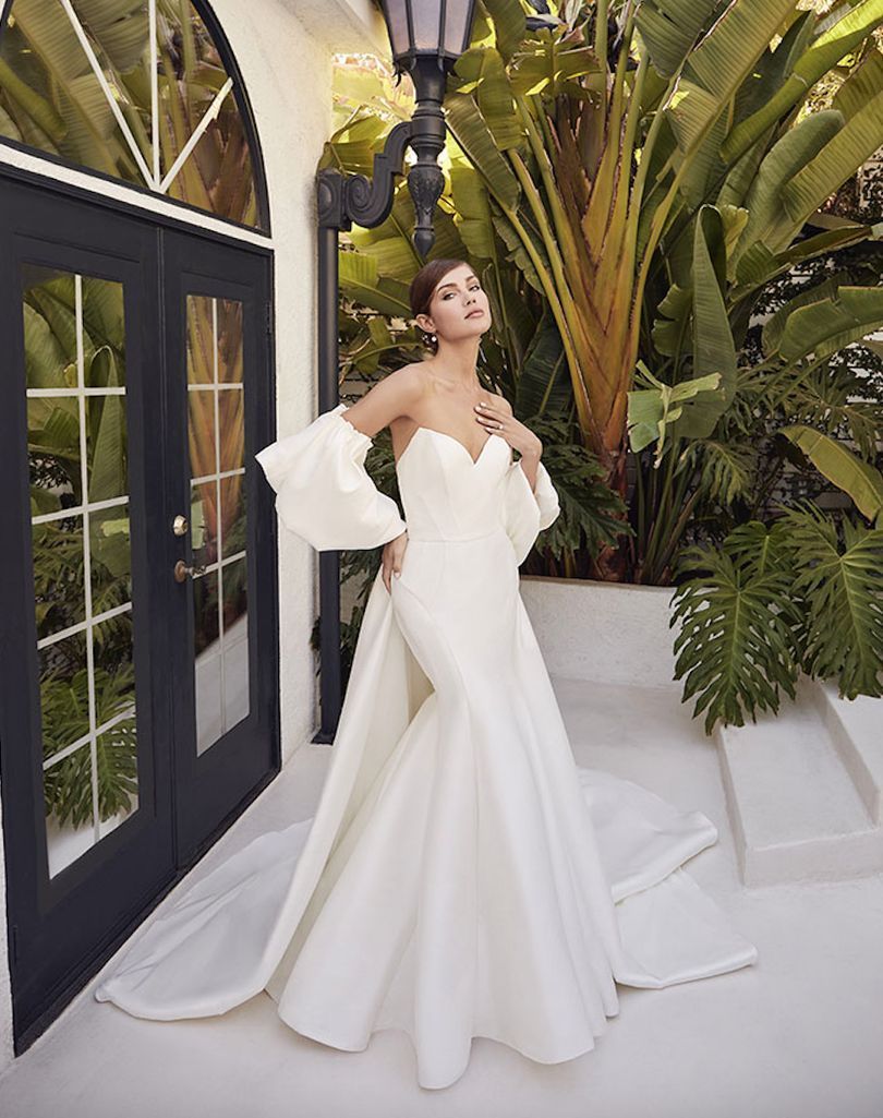 Woman in white strapless wedding gown with detachable sleeves, posing outdoors.