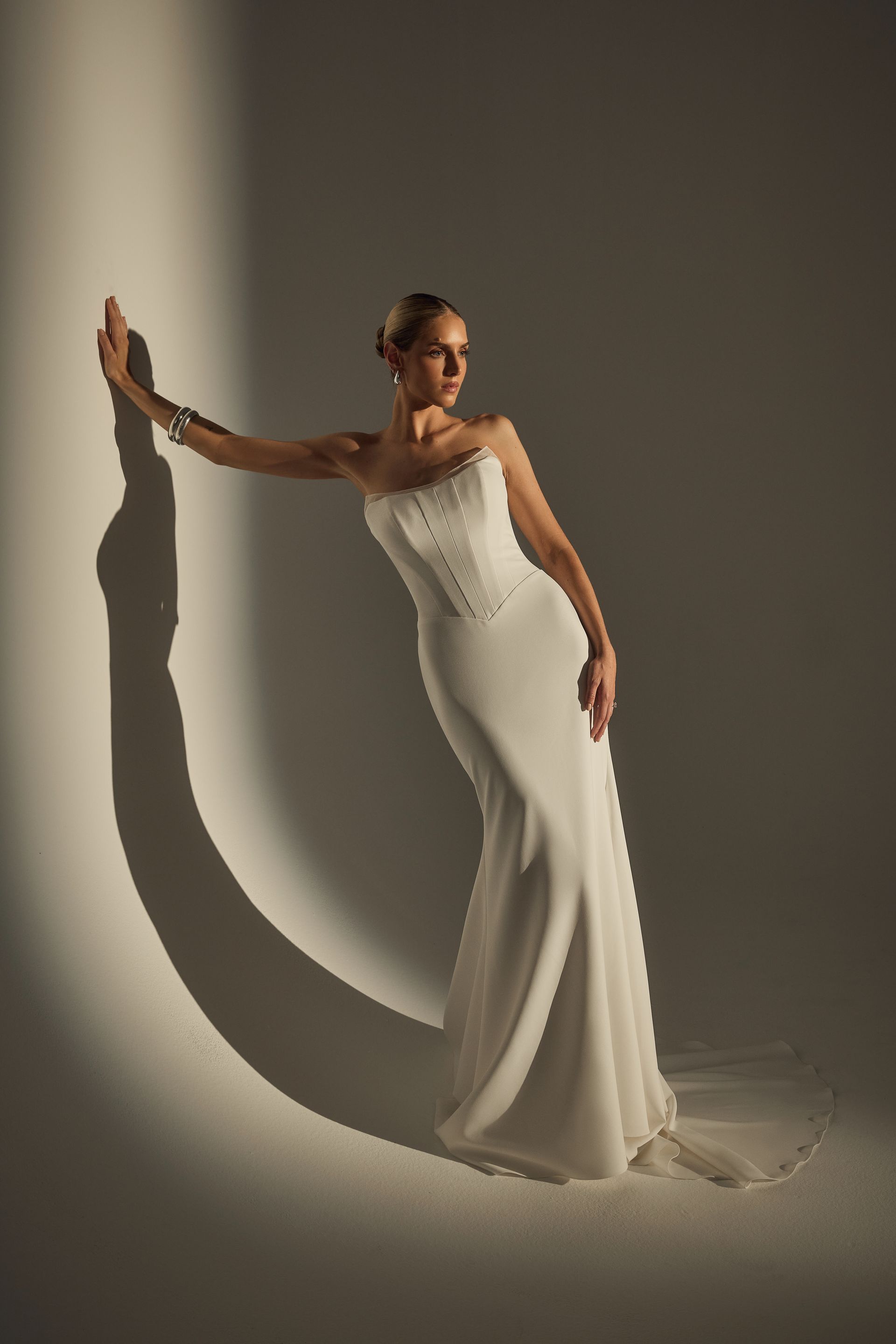 Woman in white strapless wedding dress, leaning against wall, shadow cast.