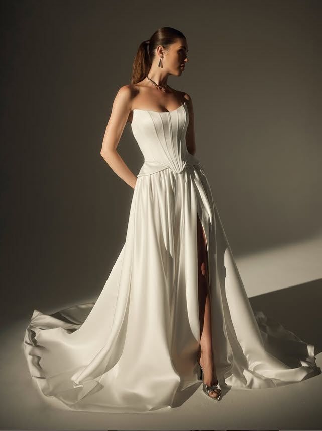 Woman wearing a white strapless wedding gown with a thigh-high slit, posing in studio light.