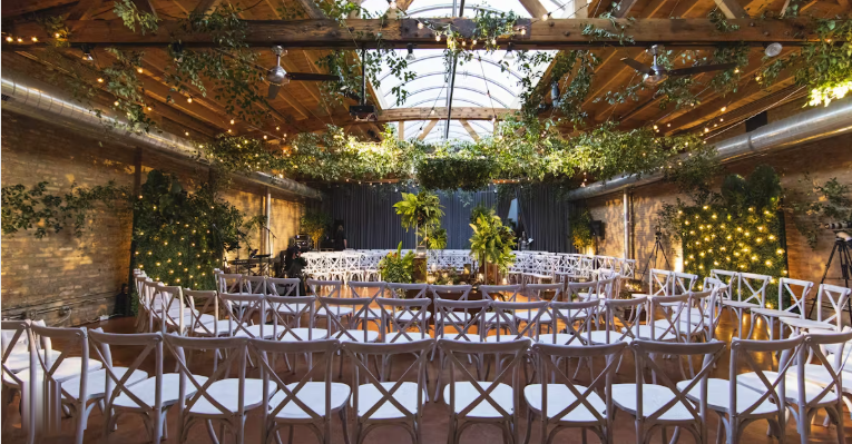 An elegant wedding venue with circular seating. Decorated with greenery, lights, and white chairs.
