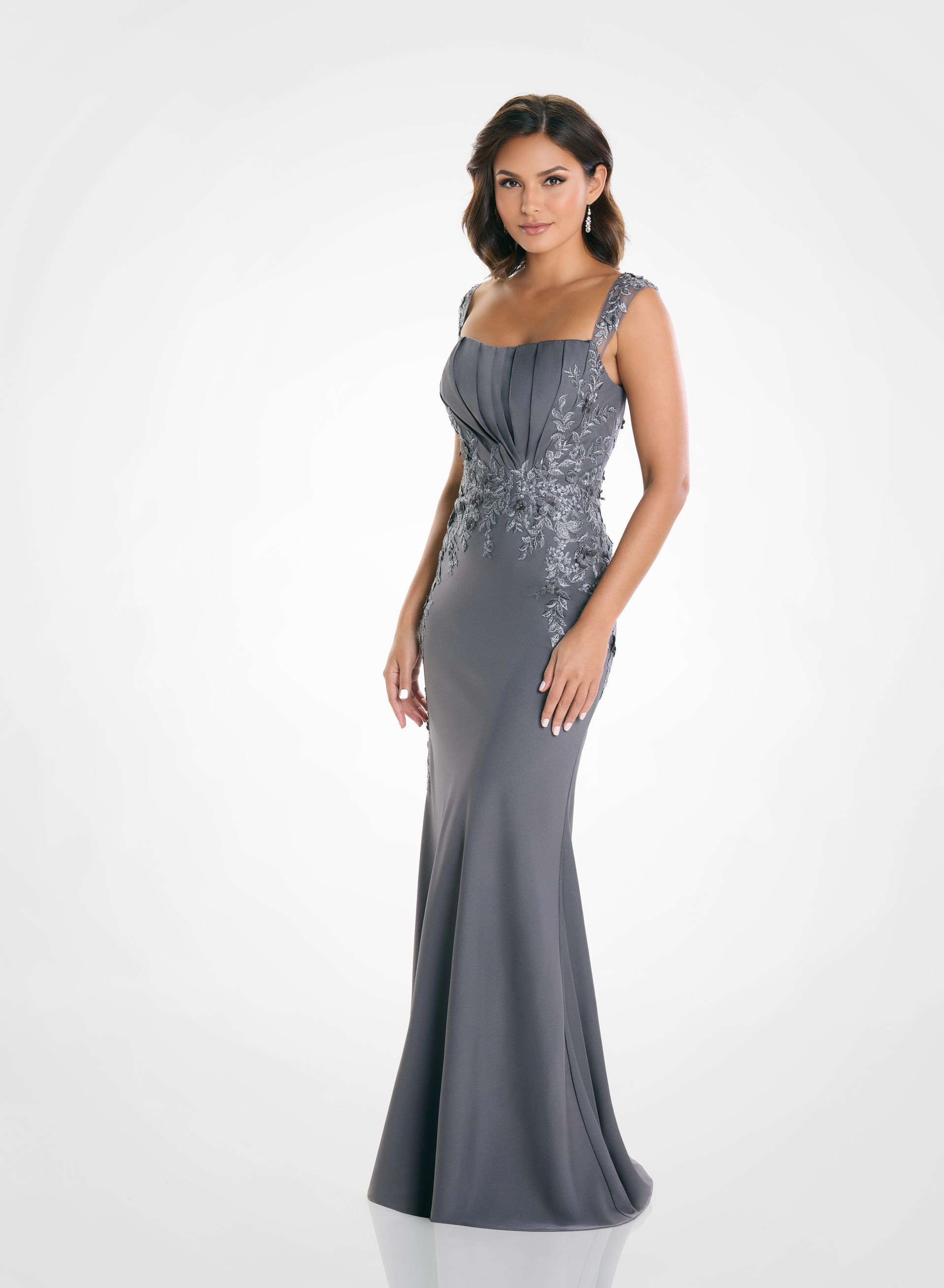 Woman in a gray, formal gown posing against a white backdrop. Dress features embellished bodice and mermaid skirt.