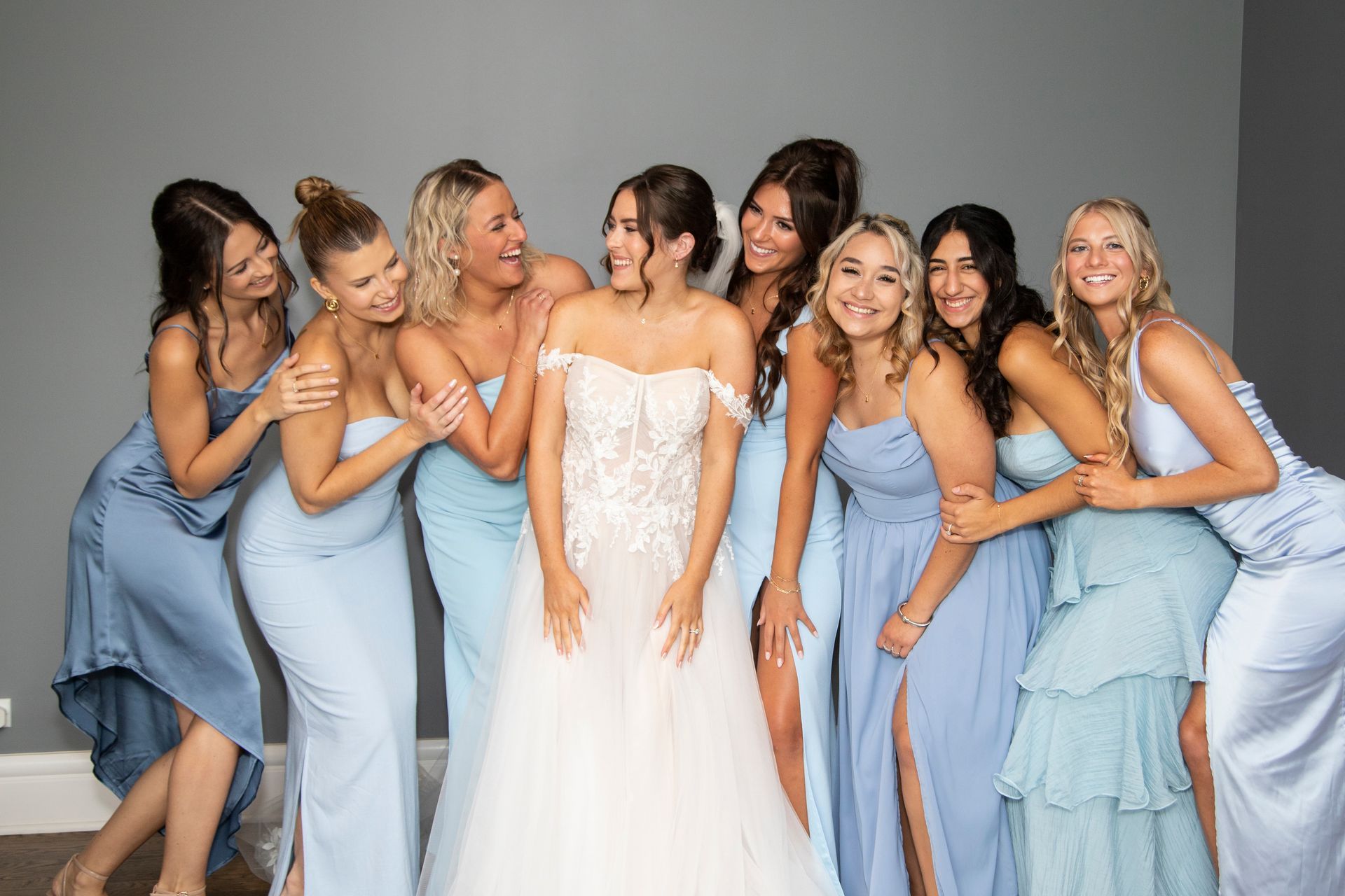 Bride in white gown surrounded by bridesmaids in blue dresses, smiling, inside.