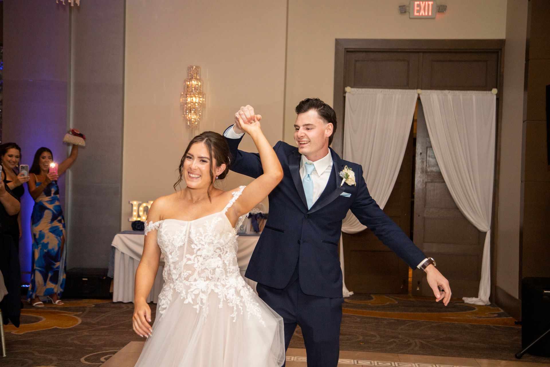 Bride and groom dancing at wedding reception. She wears a white gown, and he wears a blue suit.
