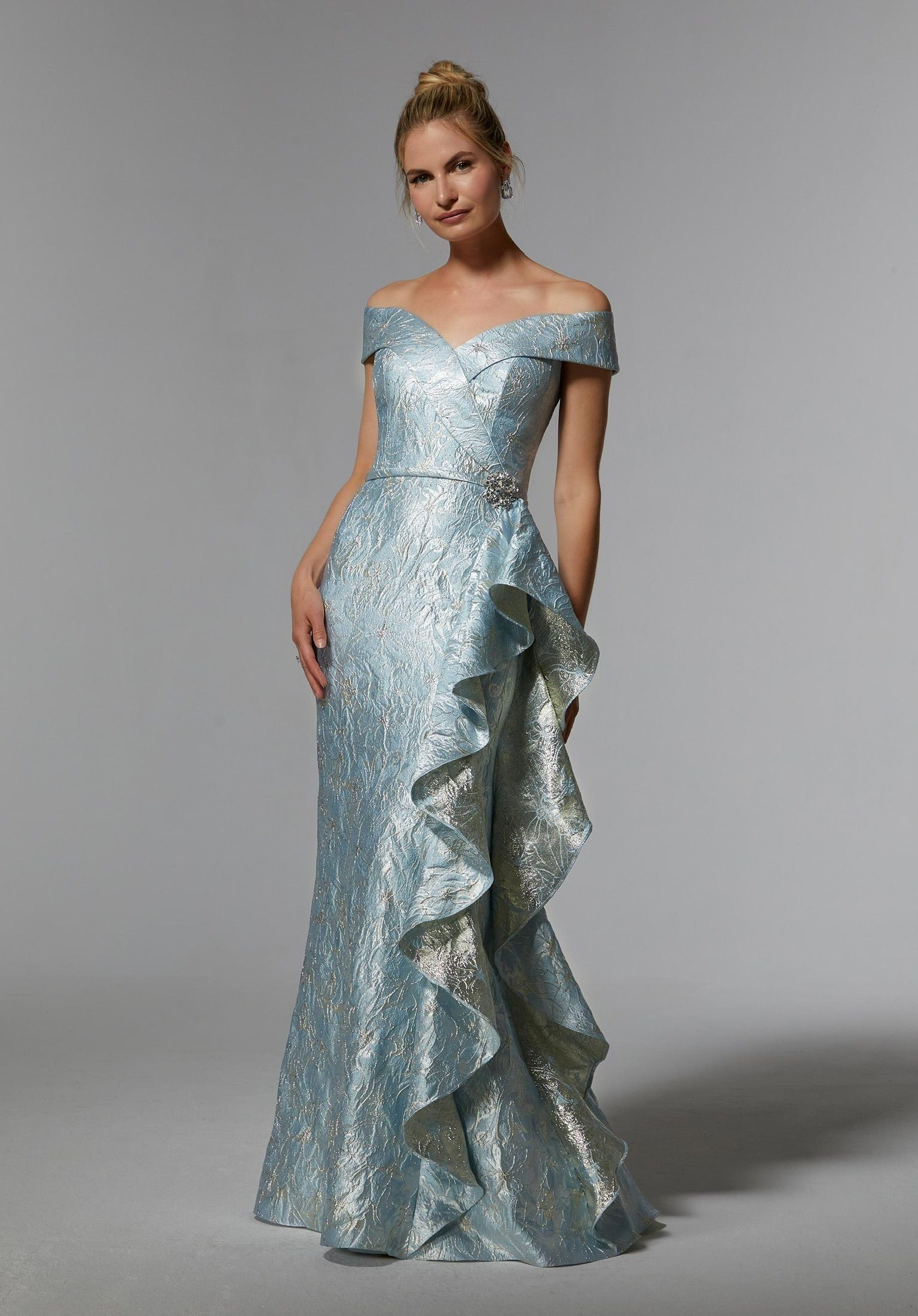 Woman in light blue off-the-shoulder gown with floral-like details and ruffled side, posing.