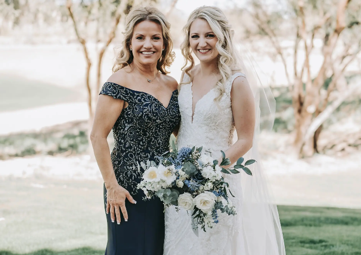 Woman in wedding dress and woman in navy gown posing outdoors, smiling.