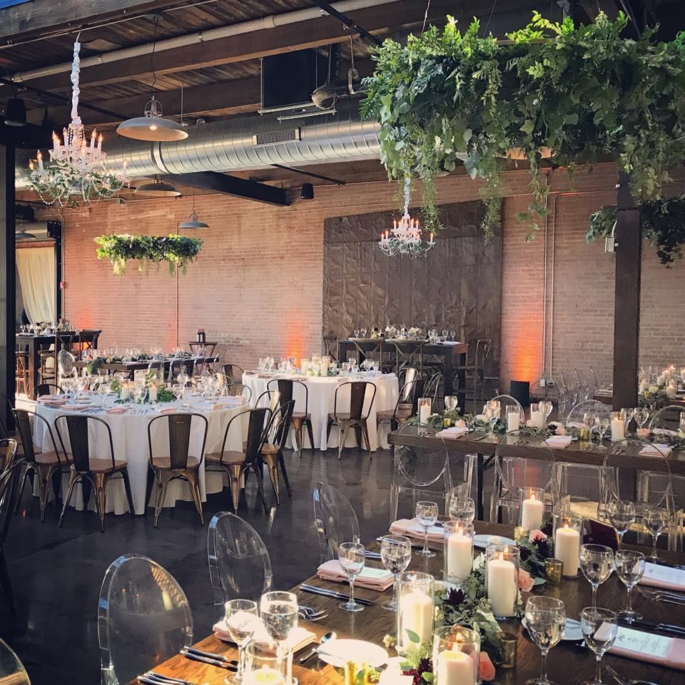 Elegant wedding reception with round tables, clear chairs, and hanging floral chandeliers.