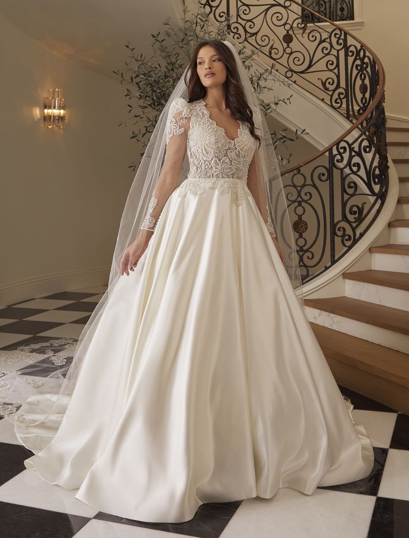 Woman in a satin wedding gown with lace bodice and veil, standing near a winding staircase.