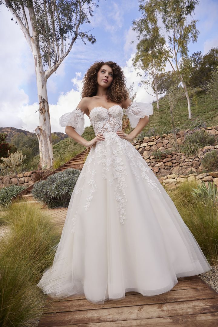 Woman in white wedding gown with puff sleeves, standing outdoors.