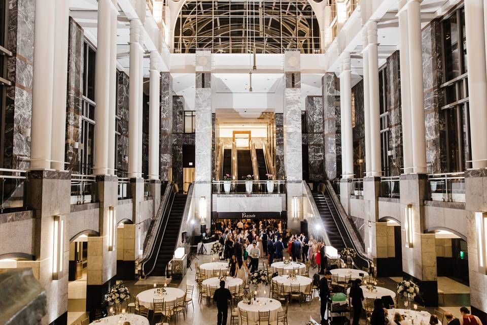 Elegant event in grand hall with tables, people, and escalators.