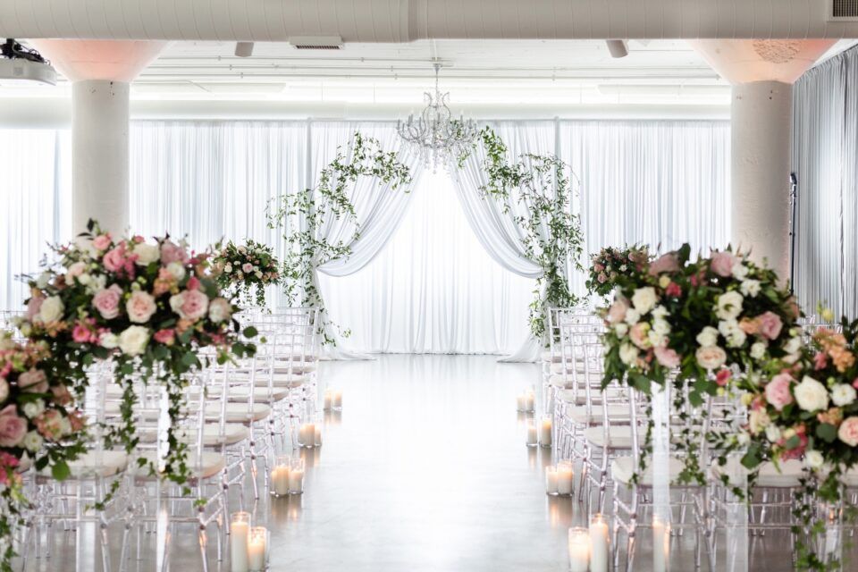 Wedding ceremony with floral arches, sheer curtains, and candlelit aisle.