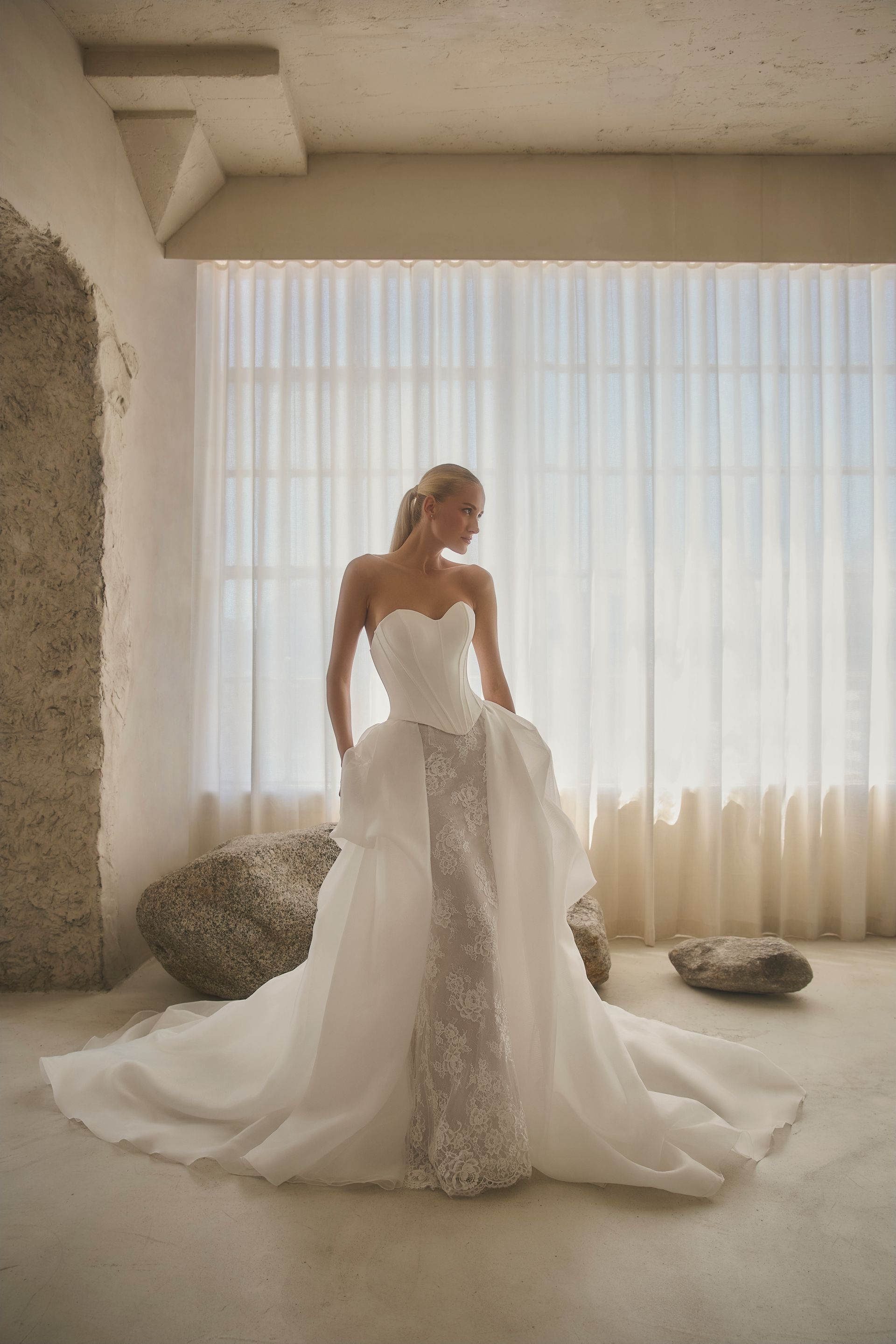 Woman in a white strapless wedding gown with train standing in front of a window.