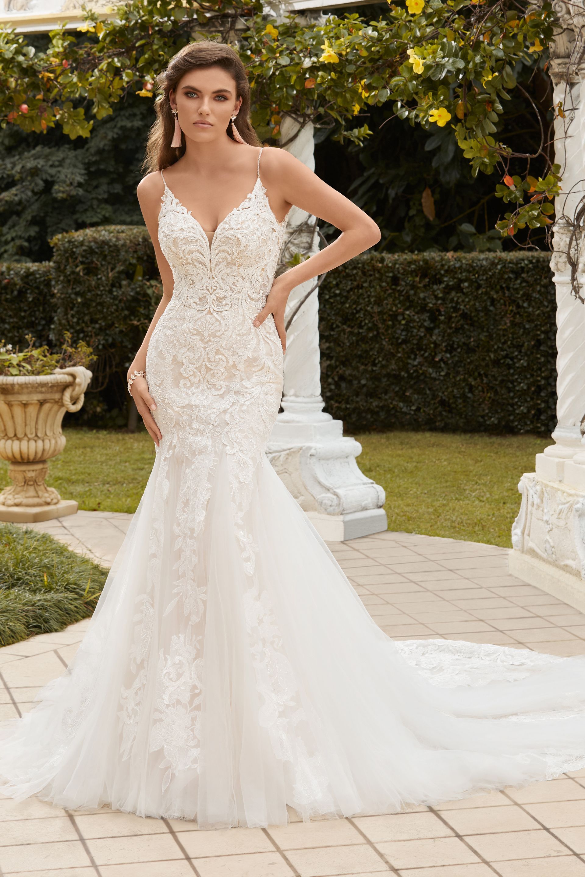 Woman in a white lace wedding dress with a train, standing outdoors.
