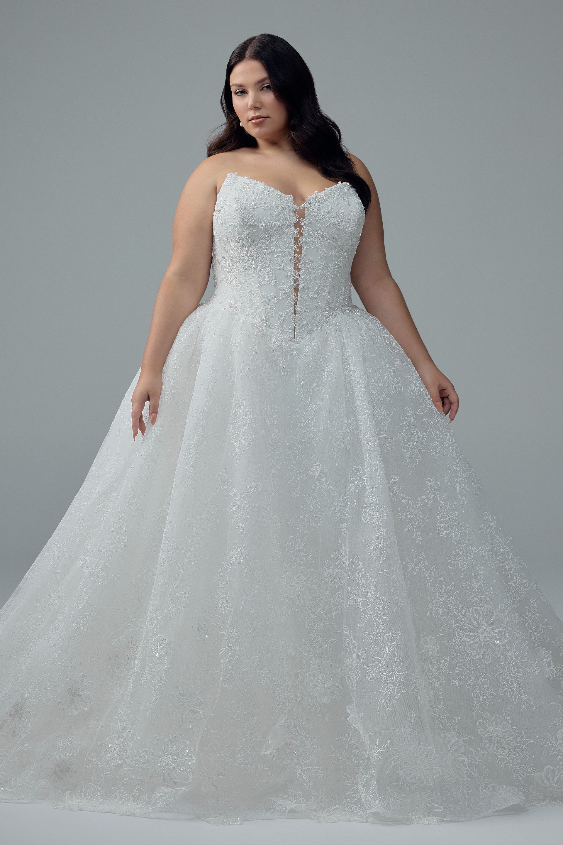 Woman in a sparkly white ballgown with a sweetheart neckline, standing in a studio with a neutral background.