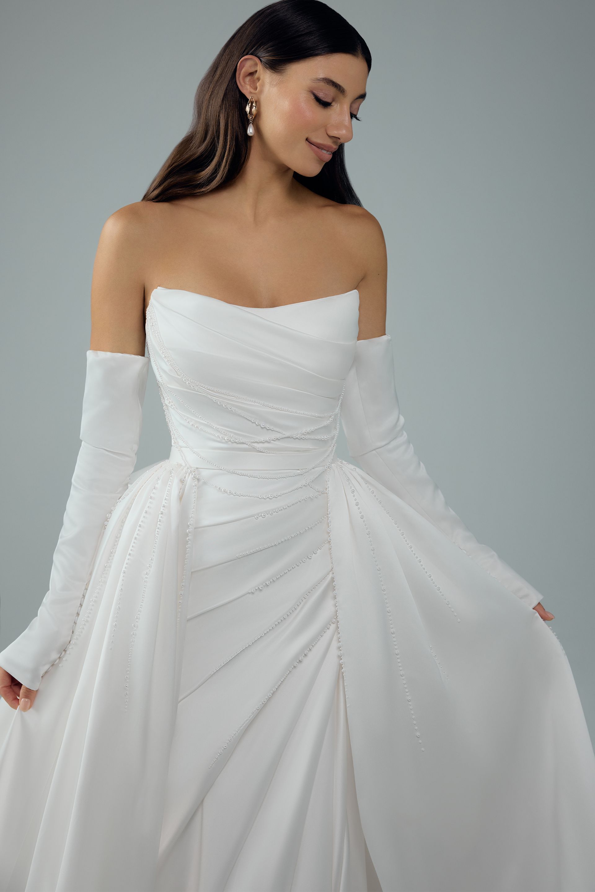 Woman in white strapless wedding gown with long, detachable sleeves, smiling, soft focus.