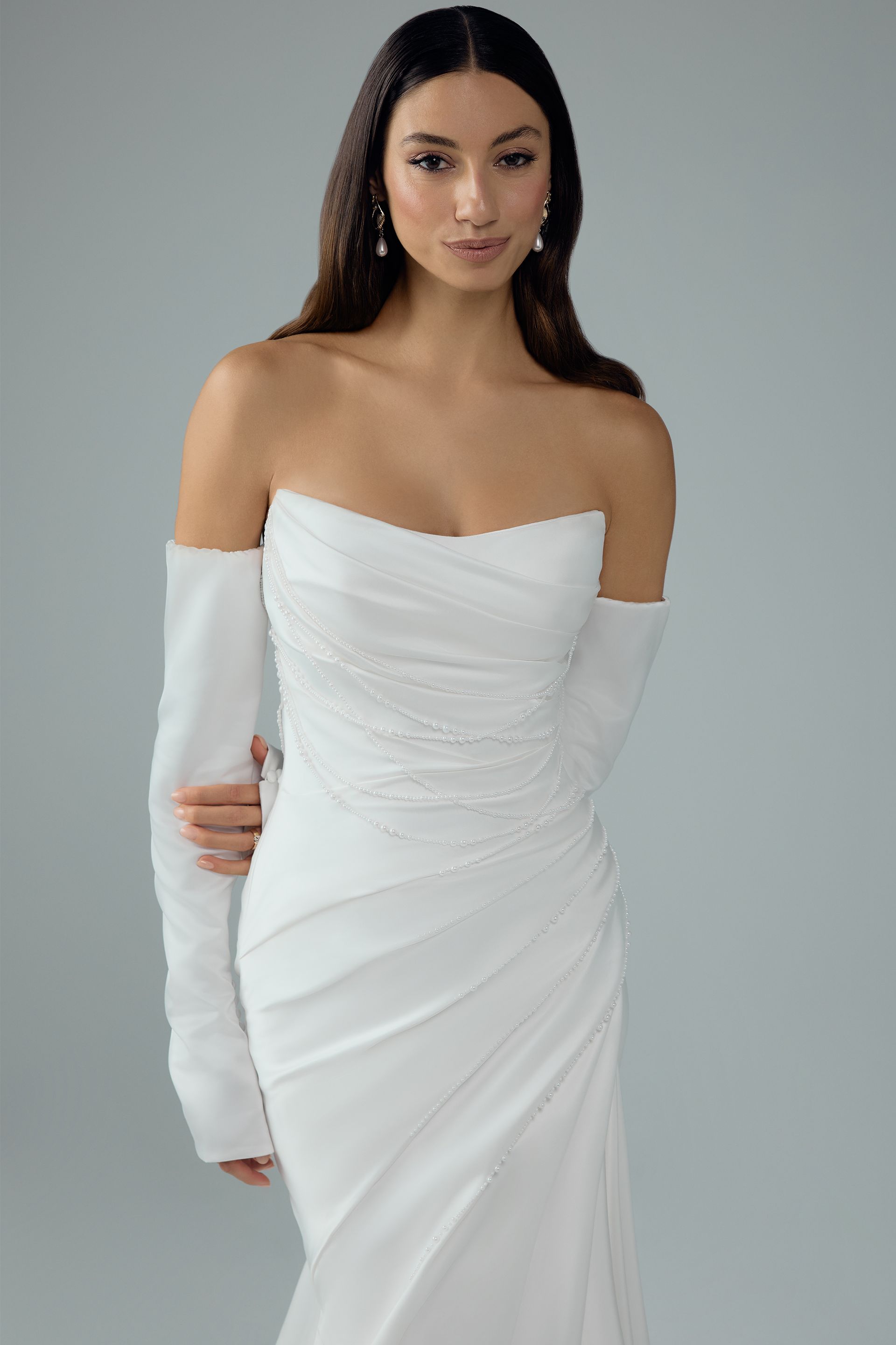 Woman in white strapless wedding dress with sheer sleeves, studio shot.