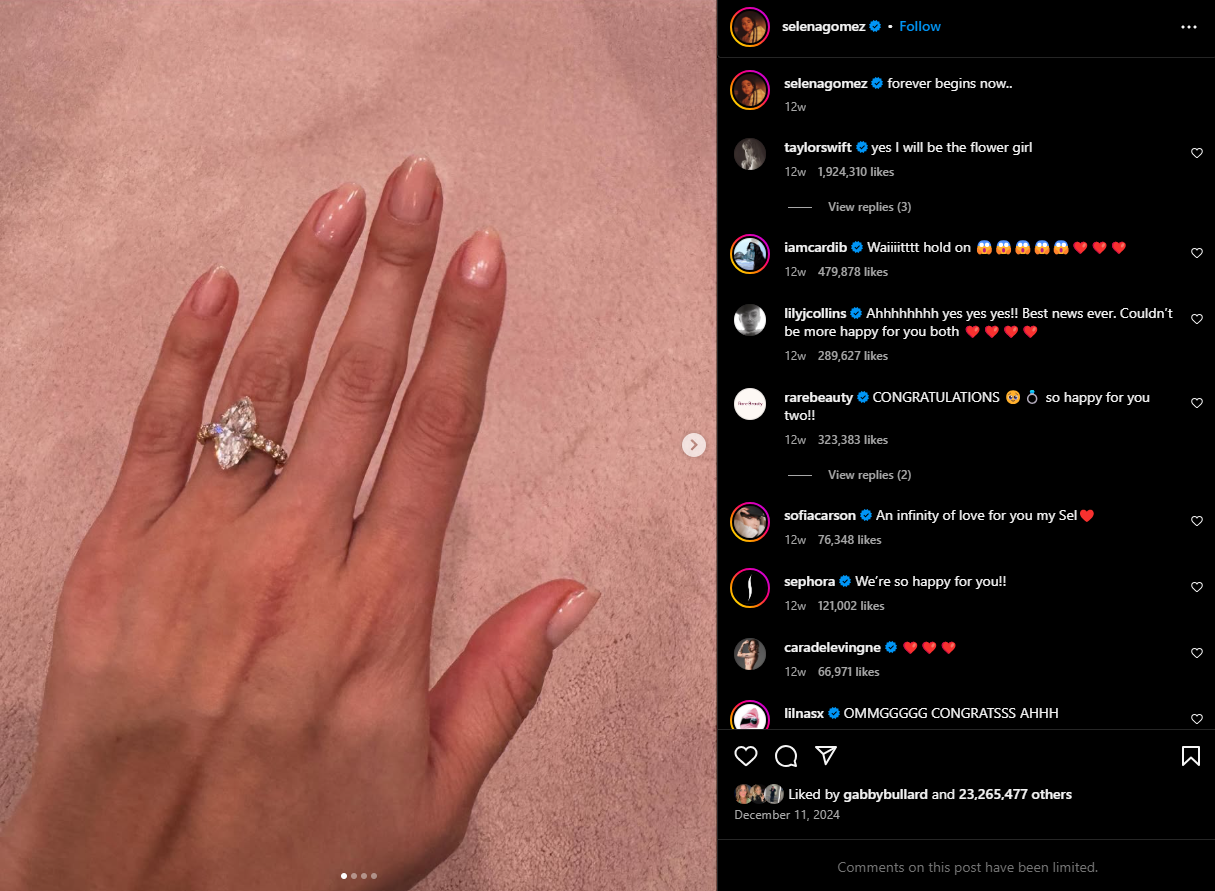 Hand wearing a large diamond engagement ring, pink manicure, on a pink surface with Instagram comments.