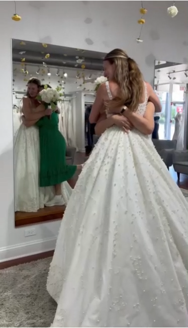 Bride in wedding dress hugs woman in green dress in bridal shop, reflected in mirror. Bride in wedding dress hugs woman in green dress in bridal shop, reflected in mirror.