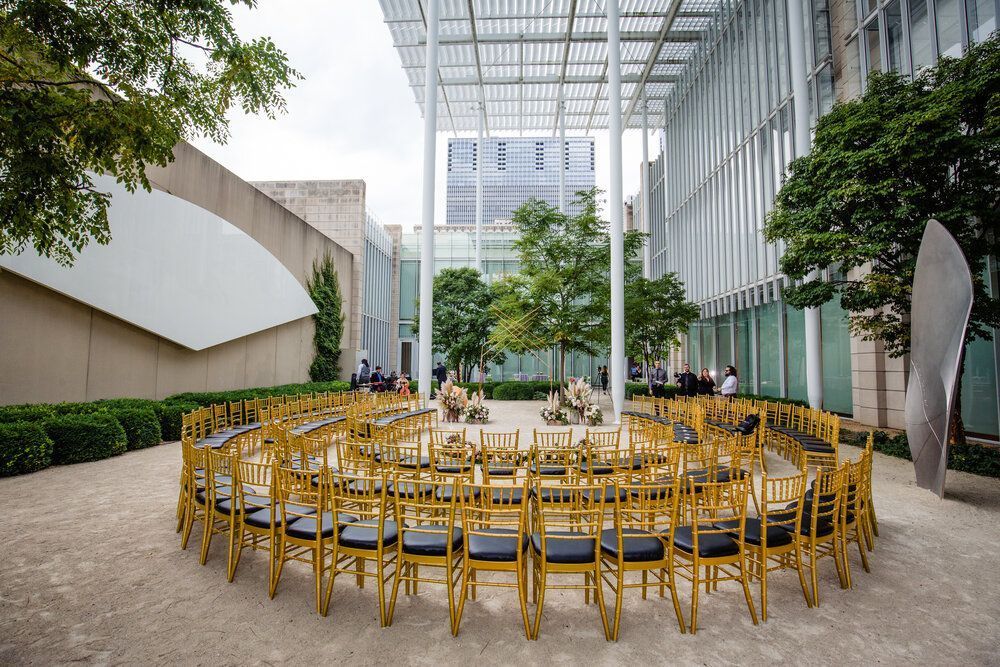 Gold chairs in a circle for an outdoor event, surrounded by trees and modern architecture.