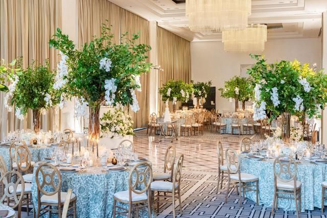 Elegant ballroom decorated for an event, featuring round tables, floral centerpieces, and chandeliers.