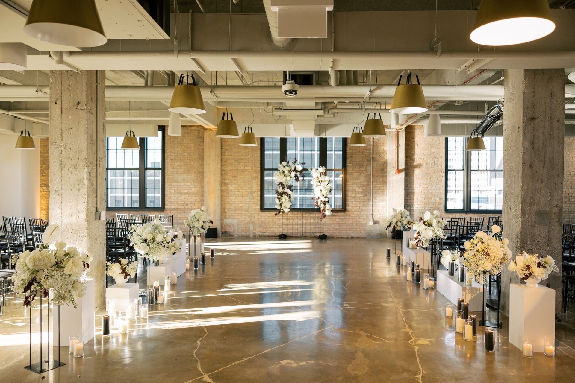 Event space with polished concrete floor, brick walls, floral arrangements, and pendant lights.