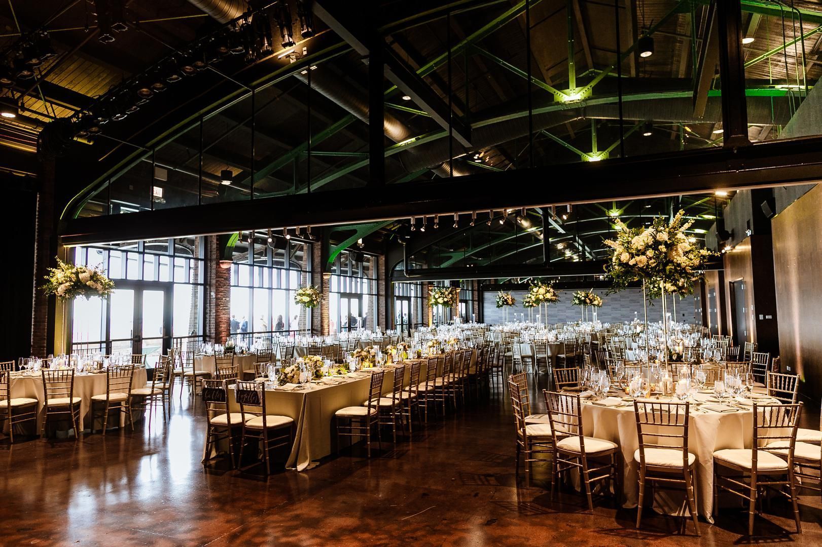Formal event space with many tables set for a banquet; brown floors, and large windows.