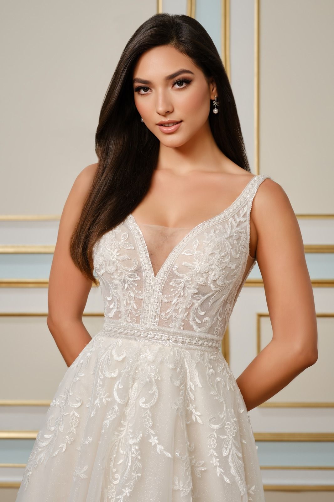 Woman in a white lace gown posing against a gold-accented wall.