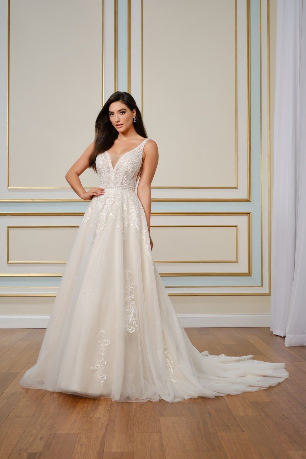 Woman in a white lace gown posing against a gold-accented wall.