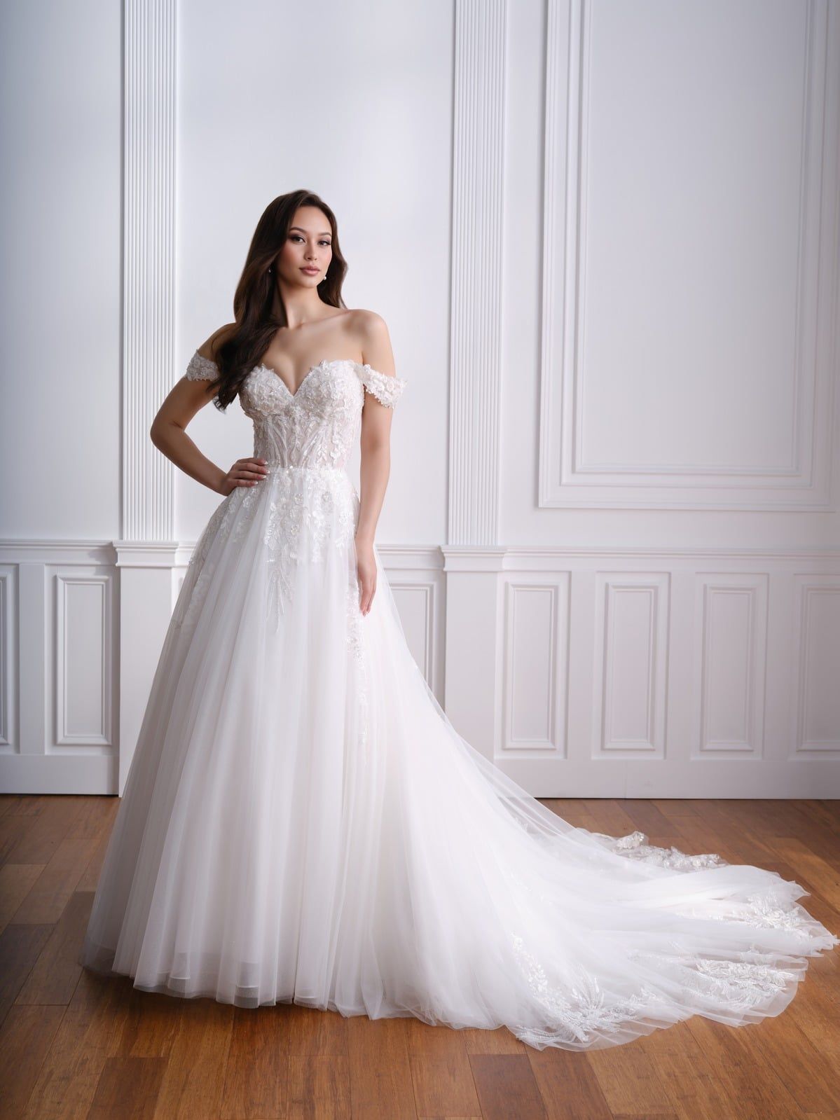 Woman in an off-shoulder white wedding gown standing in a bright paneled room.