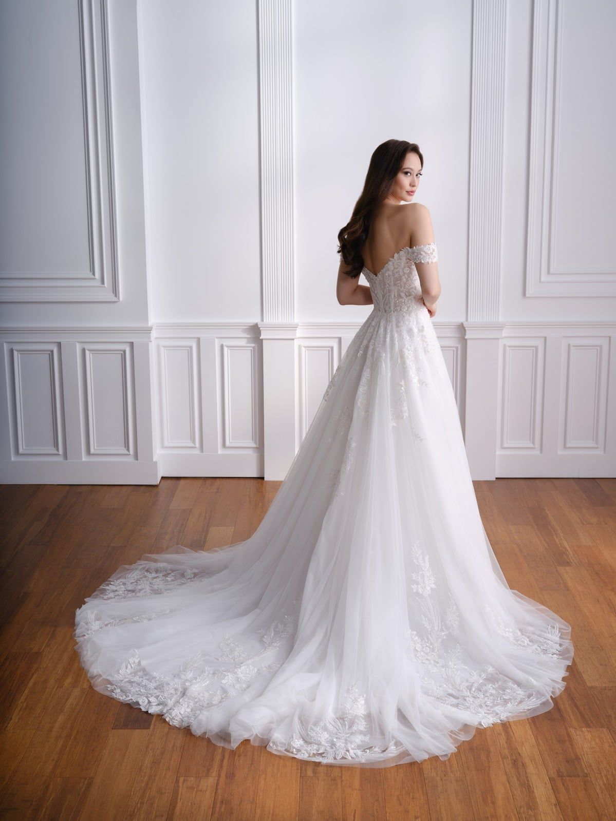 Woman in an off-shoulder white wedding gown standing in a bright paneled room.