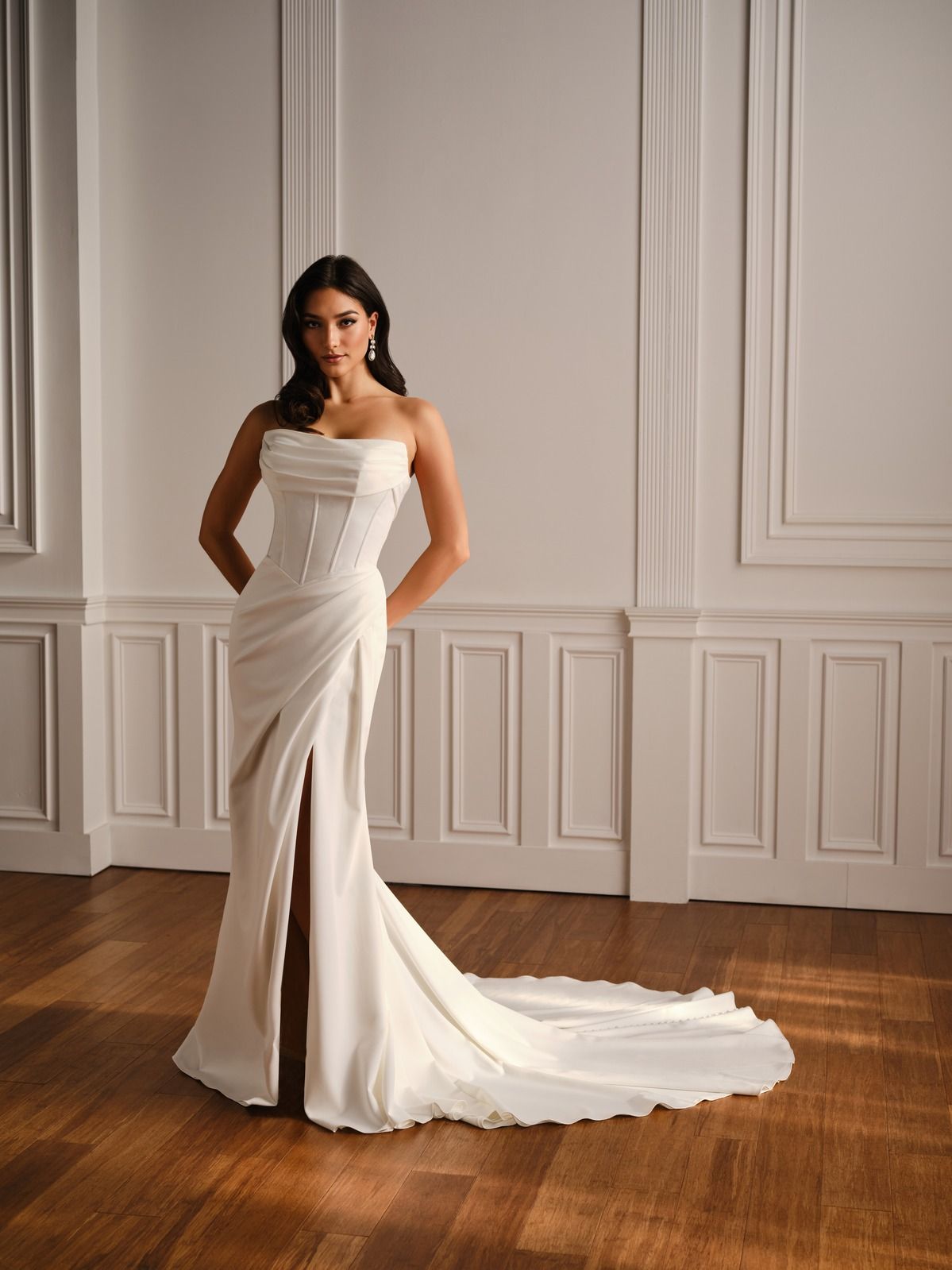 Woman in a strapless white gown posing in a paneled room with a long train on a wooden floor