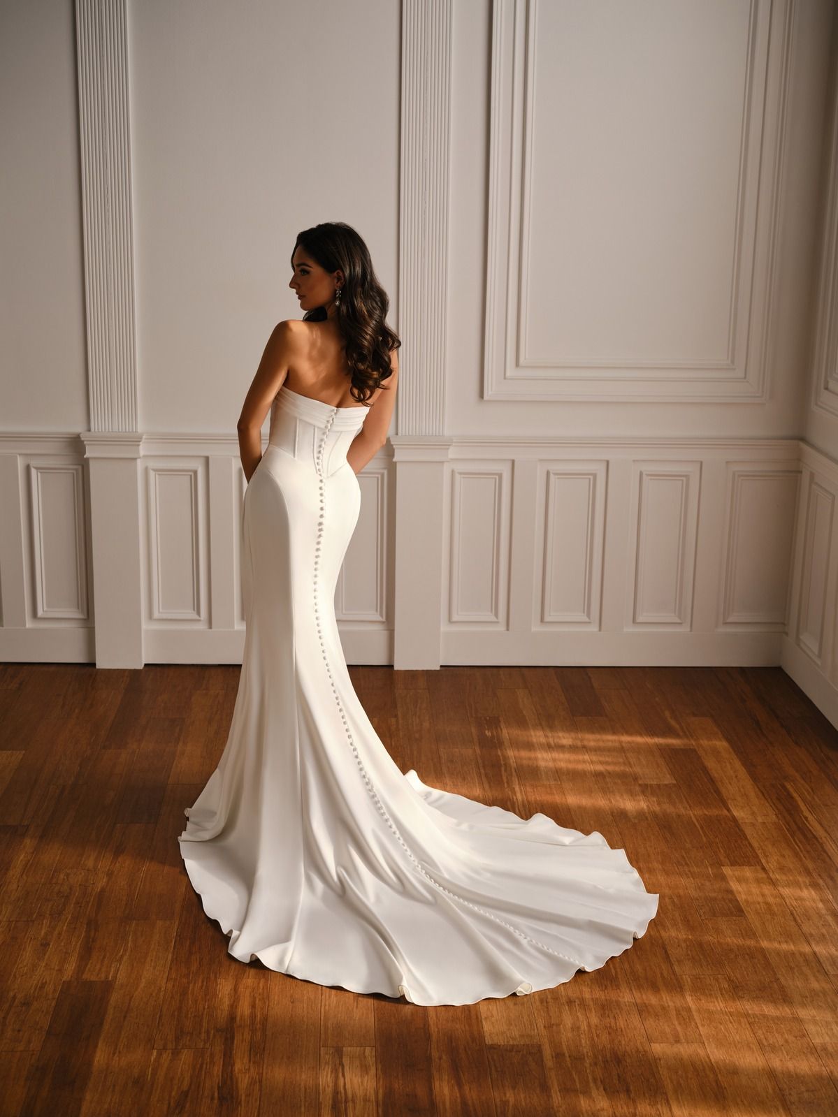 Woman in a strapless white gown posing in a paneled room with a long train on a wooden floor