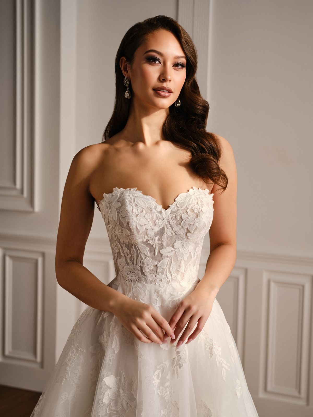 Woman in a white lace strapless gown standing in a softly lit room with paneled walls